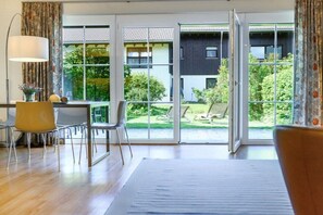 A modern room with a large sliding glass door leading to a garden, a dining area with chairs, and a table. - Holiday apartment with 3 bedrooms (Garmisch-Partenkirchen)
