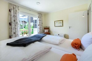 Ein Hotelzimmer mit zwei Betten, einem Fenster mit Vorhängen, einer Bettdecke in Schwarz, einer Wand-Klimaanlage und einer Tür.