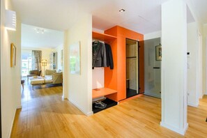 Ein Hotelzimmer mit Holzboden, einer Sitzecke mit Sofa und Sesseln sowie einem Kleiderschrank mit Kleidung.