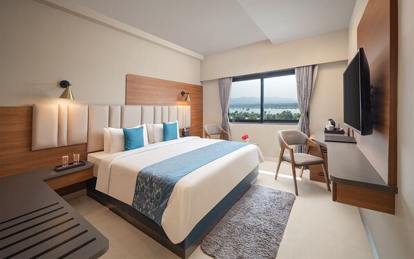 A hotel room with a large bed, a desk, a chair, a TV, and a view of the outdoors.