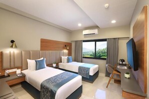 A hotel room with two beds, a desk, a chair, a TV, and a window with a view.