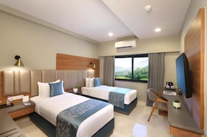 A hotel room with two beds, a desk, a chair, a TV, and a window with a view.