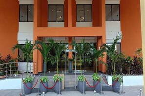 A hotel entrance with a central staircase, potted plants, and a red rope barrier.