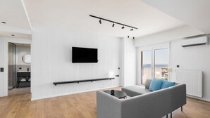 A modern living room with a grey sofa, a mounted TV, and a balcony with a view. - Celine: Apartments in the Center (Thessaloniki)