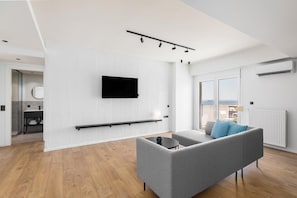 A modern living room with a grey sofa, a mounted TV, and a balcony with a view. - Celine: Apartments in the Center (Thessaloniki)
