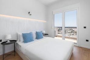 Ein modernes Schlafzimmer mit einem großen Bett, zwei Nachttischen, einer Stehlampe und Blick ins Freie durch eine Glastür.