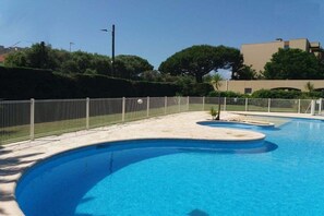 A swimming pool with a curved design, surrounded by a fence and a landscaped area with trees. - Holiday apartment with 1 bedroom (Antibes)
