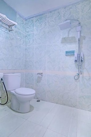 Et badeværelse med toilet, brusebad og flisebeklædt væg.
