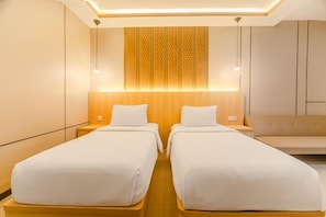 A hotel room with two single beds, a wooden headboard, and a seating area. - Five Styles Kutai Permai (Sangatta)