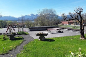 A park with a picnic area, stone planters, and a view of mountains. - in the Weber holiday home (Hopfen am See)