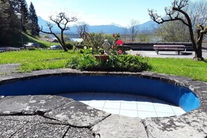 A swimming pool with a stone edge, surrounded by a grassy area with flowers and a bench. - in the Weber holiday home (Hopfen am See)