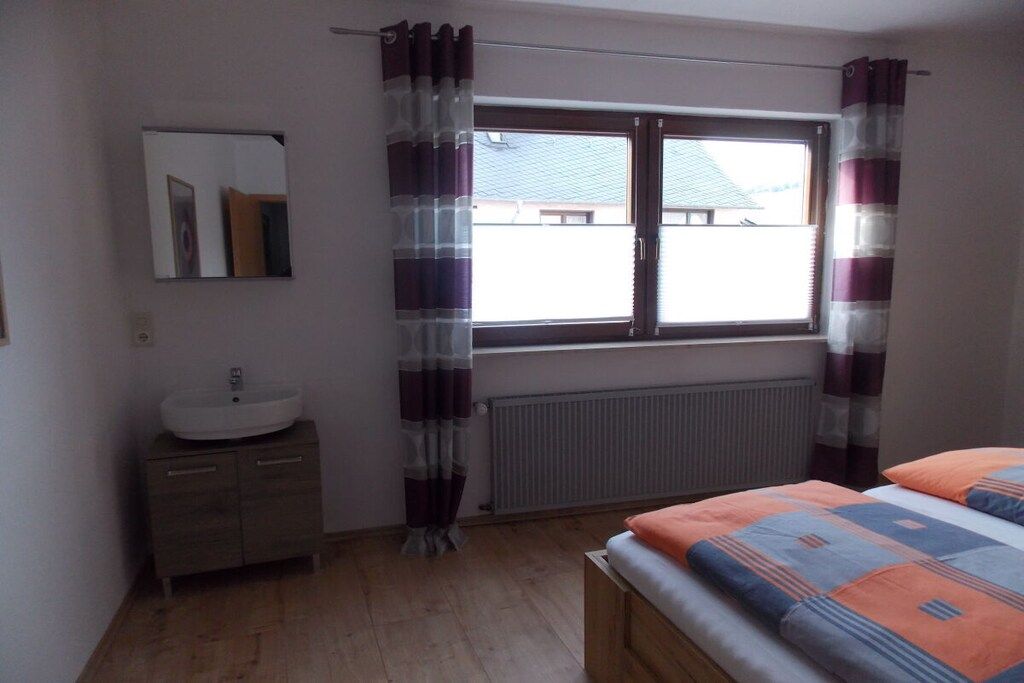 Une chambre à coucher avec un lit, une fenêtre avec des rideaux, un radiateur et un miroir au mur.