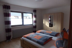 Een slaapkamer met een bed, een houten kledingkast, een raam met gordijnen en een radiator.