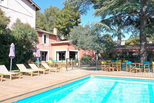 A swimming pool with lounge chairs and umbrellas, surrounded by trees and a building. - Hotel Les Jardins de Cassis (Cassis)