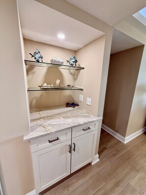 A kitchen with white cabinetry, a marble countertop, and decorative fish sculptures on shelves. - South Tower-10th Floor-2BR/2BA Custom Design & Professionally Decorated-All New! (Myrtle Beach)