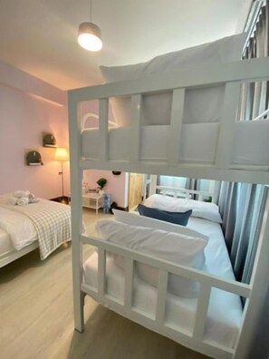A bunk bed with a white frame and a bedside table, a single bed with a white bedspread, and a lamp on a bedside table. - Triple J Hotel Trang (Trang)