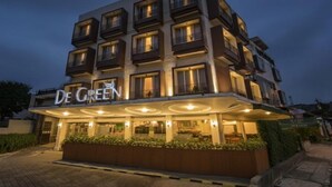 Ein mehrstöckiges Hotel mit einem gut sichtbaren 'De Green'-Schild, einem überdachten Eingangsbereich und einer gepflegten Grünanlage vor dem Gebäude.