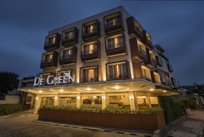 Ein mehrstöckiges Hotel mit einem gut sichtbaren 'De Green'-Schild, einem überdachten Eingangsbereich und einer gepflegten Grünanlage vor dem Gebäude.