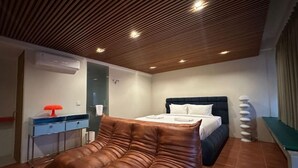 A modern bedroom with a large bed, a desk with a lamp, and a wall-mounted air conditioner. - Aksara Hotel by Aruna Group (Bandung)