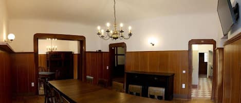 A dining area with a long wooden table, chairs, a chandelier, and wooden paneling on the walls.