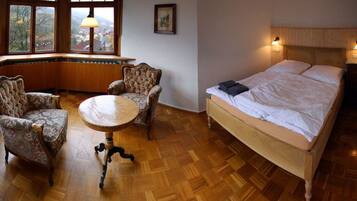 Ein Zimmer mit einem Bett, zwei Sesseln, einem runden Tisch und einem Fenster mit Blick.
