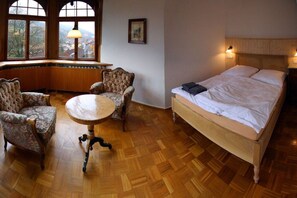 Una habitación con cama, dos sillones, una mesa redonda y ventana con vistas.