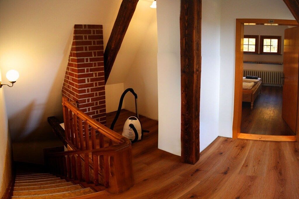 A wooden staircase with a brick fireplace, a vacuum cleaner, and a bed in a room with wooden flooring and a radiator.