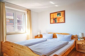 Een enkel bed met een houten hoofdbord en voetenbord, een nachtkastje met een lamp, en een raam met gordijnen.