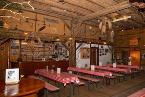 Ein Restaurantinneres mit Holzbalken, rot-weiß karierten Tischen und einer Bar mit Regalen voller Flaschen.