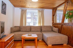 Ein gemütliches Wohnzimmer mit einer Eckcouch, Holzdielenboden, einem kleinen Tisch und einem Fernseher.
