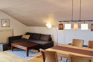 A cozy living room with a sofa, coffee table, and dining table with chairs. - Apartment AusZeit in Finning (Finning)