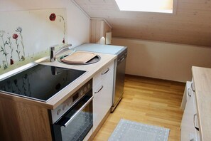A compact kitchen with a built-in stove, a dishwasher, and a small countertop. - Apartment AusZeit in Finning (Finning)