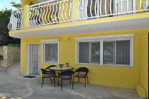 A yellow building with a balcony, a round table with chairs, and two windows. - Spacious modern apartment with big patio and sea view (Slatine)