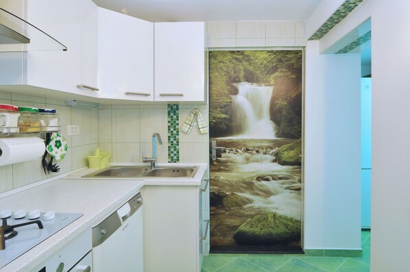 Een keuken met witte kastjes, een spoelbak en een spatwand met groene en witte tegels.
