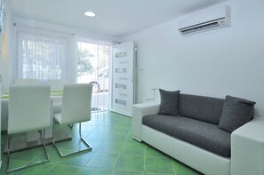 A modern living room with a white sofa, a dining table with chairs, and a large window with sheer curtains. - Spacious modern apartment with big patio and sea view (Slatine)