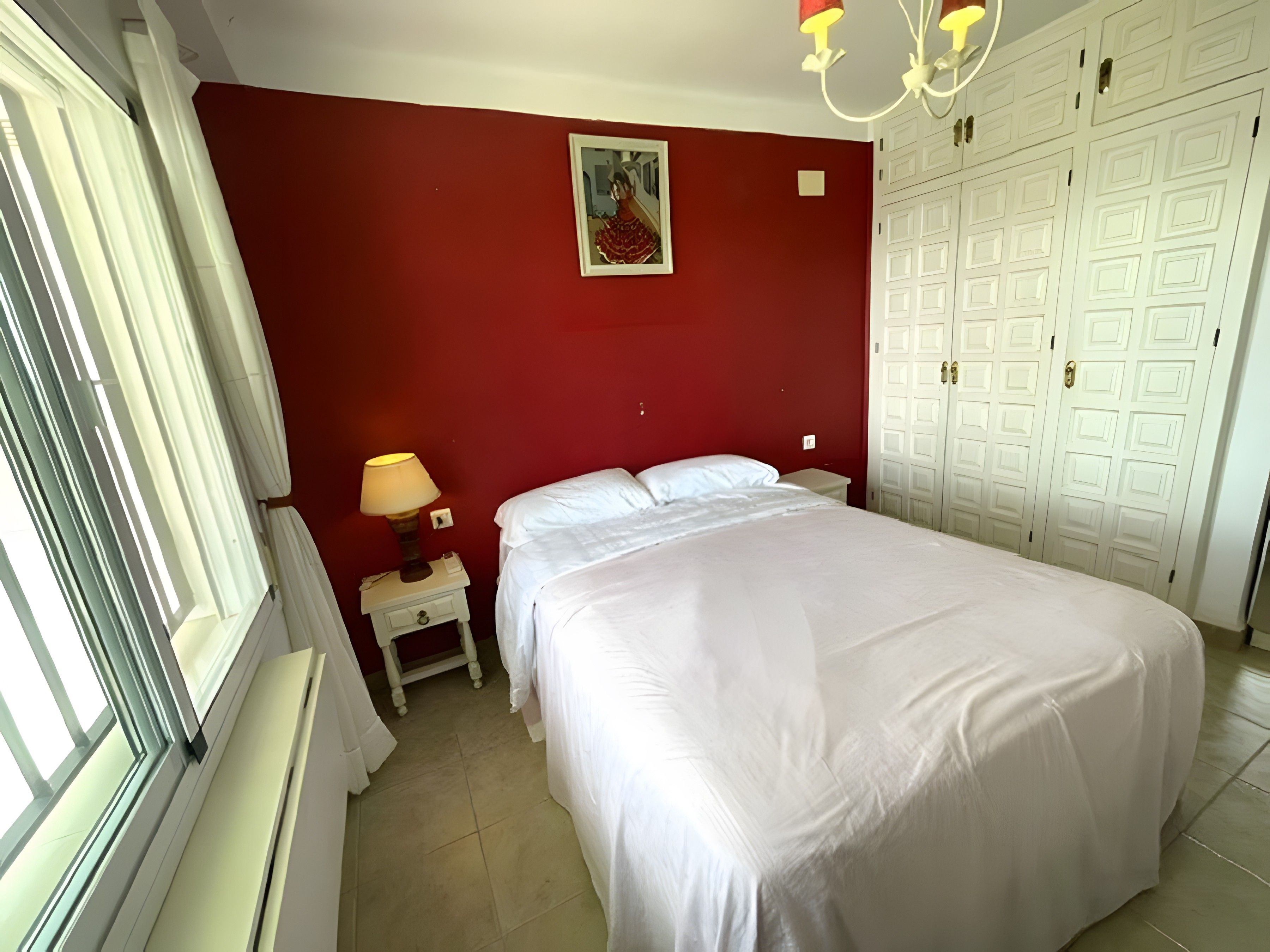 A bedroom with a bed, a nightstand, a lamp, a painting, and a wardrobe.