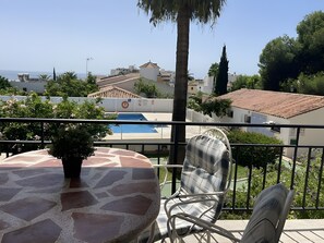 A balcony with a table and chairs, overlooking a swimming pool and buildings. - Apartment 'In Parador Area Nerja' with Sea View, Shared Pool and Air Conditioning (Nerja)
