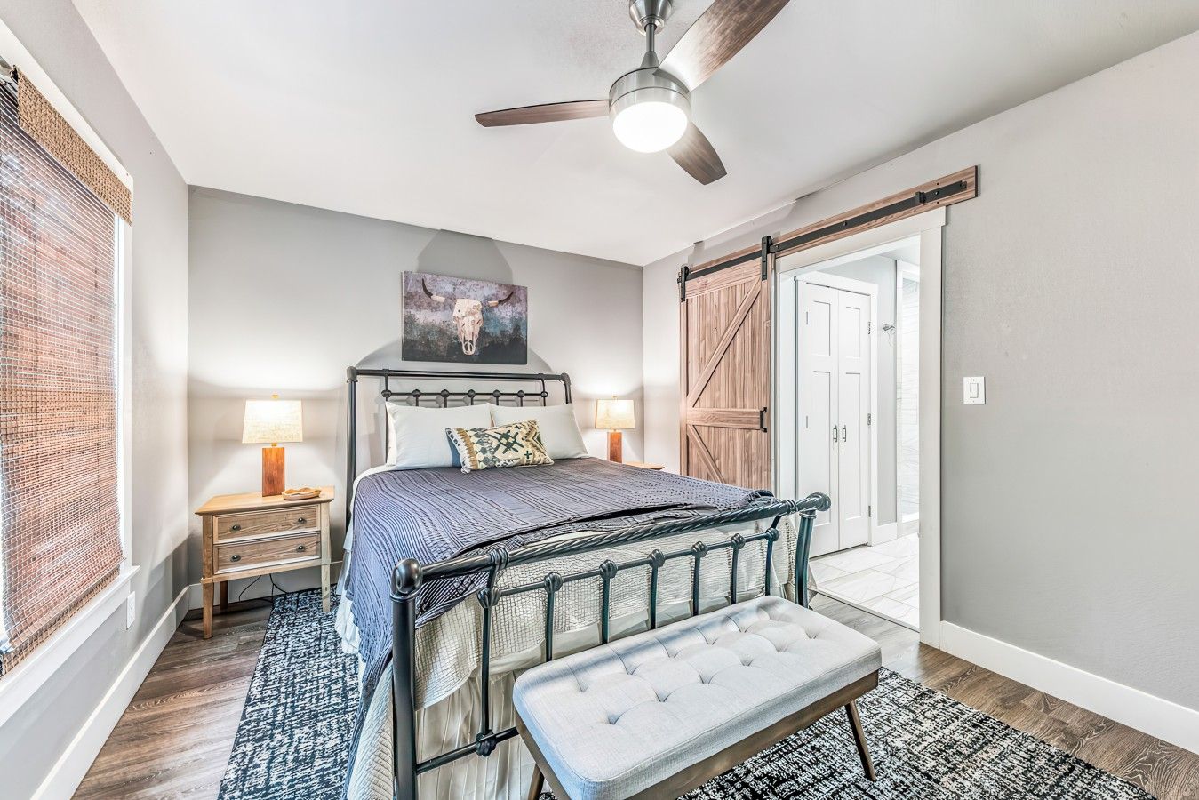 Une chambre à coucher avec un lit, des tables de chevet, un banc, un ventilateur de plafond et une porte.