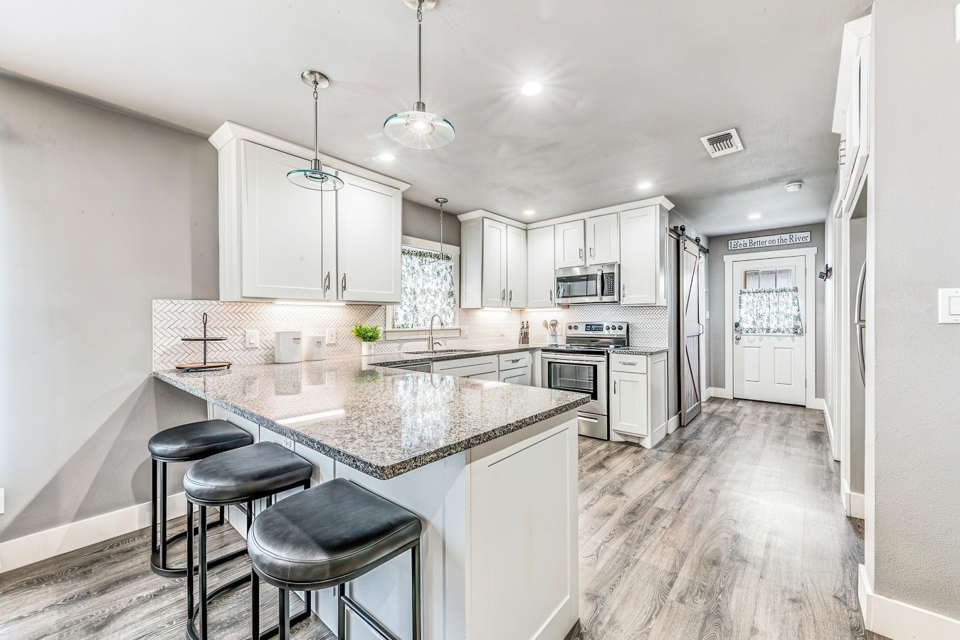 A modern kitchen with a large island, bar stools, stainless steel appliances, and a herringbone-patterned backsplash.