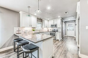 A modern kitchen with a large island, bar stools, stainless steel appliances, and a herringbone-patterned backsplash. - Gruene Road Cottage - New Braunfels (New Braunfels)