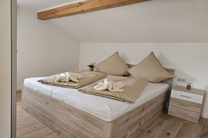 A bedroom with a wooden bed frame, two pillows, a bedside table, and a nightstand. - Holiday apartment Breitenberg (Hopferau)