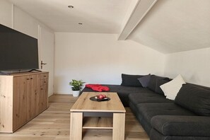 A modern living room with a dark grey sofa, a wooden coffee table, a television on a cabinet, and a potted plant. - Holiday apartment Breitenberg (Hopferau)