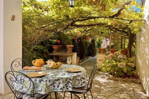 An outdoor dining area with a table set for two, surrounded by greenery and a pergola. - Holiday apartment with 1 bedroom (Antibes)