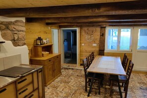 Interior em madeira com mesa de jantar, cadeiras, cozinha com armários e uma parede de pedra.