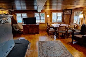 L’intérieur d’un chalet accueillant, avec un plancher en bois, un téléviseur, une table à manger avec des chaises et une cheminée.