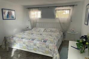 Een slaapkamer met een bed, nachtkastje, raam met gordijnen en een aan de muur hangend schilderij.