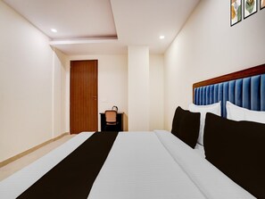 A hotel room with a large bed, a wooden door, a small table with a chair, and a wall-mounted artwork. - Deluxe Preet Vihar Metro Station (New Delhi)