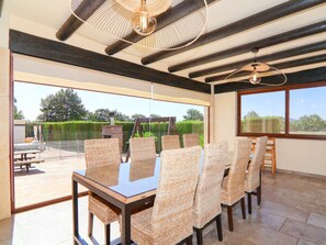 A dining area with a glass table and wicker chairs, large windows, and a view of the outdoors. - Villa in Sa Pobla With Swimming Pool (Sa Pobla)