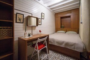 Un dormitorio pequeño con una cama individual, un escritorio con silla, un espejo y una pequeña estantería con objetos decorativos.