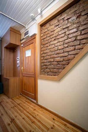 A hallway with wooden flooring, a wooden door, and a brick wall.